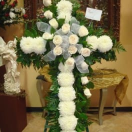 White floral cross arrangement with roses and ribbon on an easel