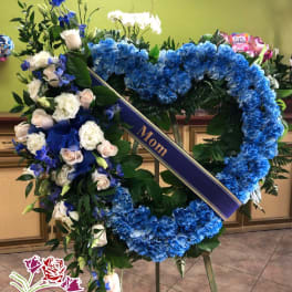 Heart-shaped funeral wreath with blue hydrangeas and white roses on an easel