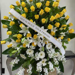 Large funeral spray of yellow roses and white lilies with a memorial ribbon