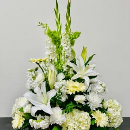 White lilies and pale yellow daisies in a wicker basket arrangement