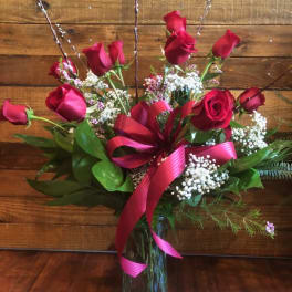 Red roses arranged in a glass vase with a pink ribbon