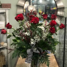 Red roses arranged in a clear glass vase with a striped ribbon