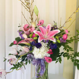 Pink lilies and mixed flowers in a glass vase with a purple ribbon