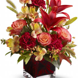 Mixed bouquet of red lilies, pink roses, and carnations in a glass vase