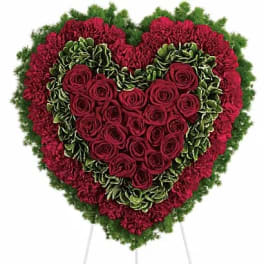 Heart-shaped floral spray with red roses and carnations on a stand