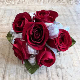 Compact cluster of red roses with silver and white ribbon in a round posy on a light wood surface