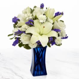 White lilies and roses arranged in a blue glass vase with purple accents