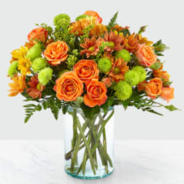 Orange roses and green chrysanthemums in a clear glass vase