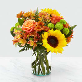 Bouquet of sunflowers, roses, and orange flowers in a glass vase