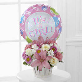 Pink and white flower arrangement with a "It's a Girl!" balloon