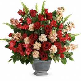 Red roses and peach carnations in a gray urn vase