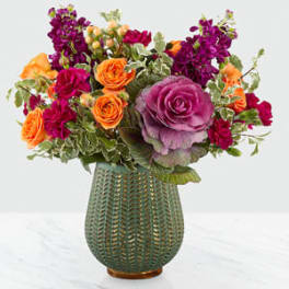 Colorful bouquet of roses and purple blooms in a textured green vase