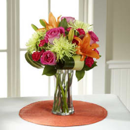 Bouquet of pink roses, orange lilies, and green spider mums in a glass vase