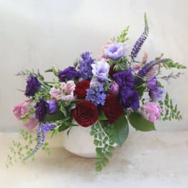 Mixed bouquet of red, pink, and purple flowers in a white vase