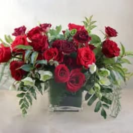 Red rose arrangement in a square vase with trailing greenery