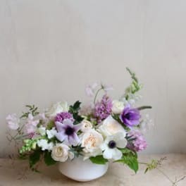 Low floral arrangement in a white bowl with white and purple blooms