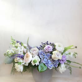 Low floral arrangement in a gray vase with white, lavender, and blue blooms