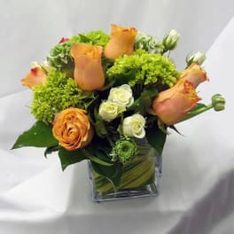 Orange roses and green blooms arranged in a square glass vase