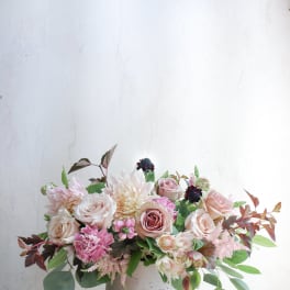 Low floral arrangement of blush roses and pale blooms in a white vase