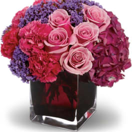 Pink roses and purple flowers arranged in a clear square vase