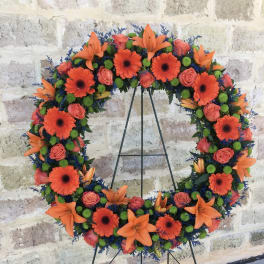 Circular floral wreath with orange lilies, gerbera daisies, and pink roses on a stand