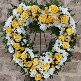 Heart-shaped floral wreath with yellow roses and white daisies on a stand