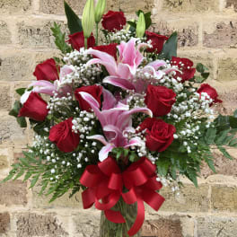 Red roses and pink lilies in a glass vase with a red ribbon