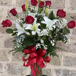 Red roses and white lilies in a clear glass vase with a red ribbon
