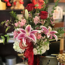 Bouquet of red roses and pink lilies in a tall vase with a red ribbon