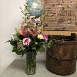 Tall mixed flower arrangement in a glass vase with a birthday balloon