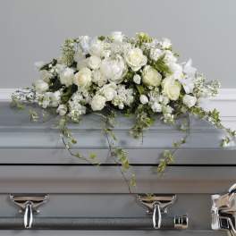 White floral casket spray with trailing ivy on a gray casket