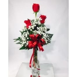 Red roses arranged with white baby's breath in a clear vase with a red ribbon