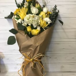 Yellow and white bouquet wrapped in brown paper with a raffia tie