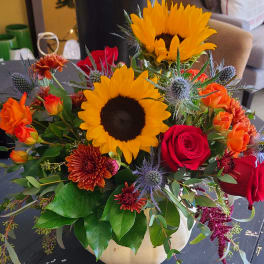 Mixed bouquet with sunflowers, roses, and orange blooms in a white vase