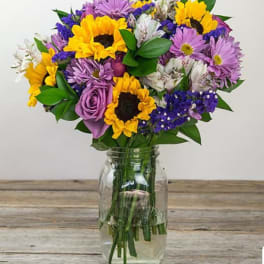 Mixed bouquet of sunflowers, purple daisies, and white blooms in a glass jar