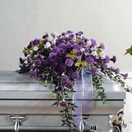 Purple floral spray draped over a silver casket with a lavender ribbon