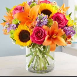 Bouquet of orange lilies, pink roses, and sunflowers in a glass vase