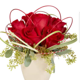 Red roses arranged in a cream vase with decorative loops