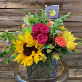 Bright mixed bouquet with sunflowers, pink roses, and yellow blooms in a glass vase.