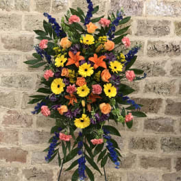 Standing floral spray with orange roses, yellow daisies, and blue accents