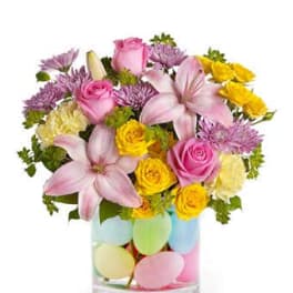 Pink and yellow flowers in a clear vase with pastel egg decorations