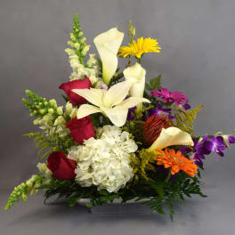Mixed bouquet with white lilies, red roses, and colorful daisies in a low container