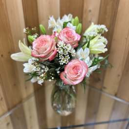 Pink roses and white lilies with small white blossoms arranged in a clear glass vase.