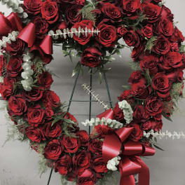 Heart-shaped wreath of red roses with ribbon bows on a stand