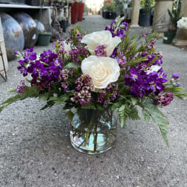White roses and purple flowers arranged in a glass vase