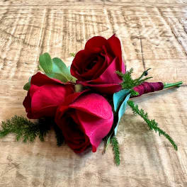 Small bouquet of red roses with greenery on a wooden surface