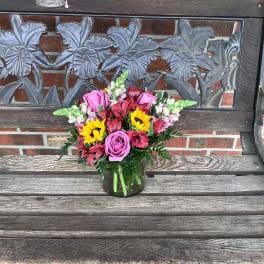 Mixed bouquet of pink roses, sunflowers, and red flowers in a glass vase