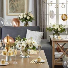White floral arrangements in glass vases on tables with balloons and desserts