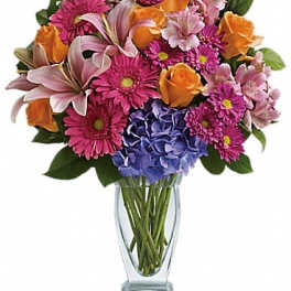 Mixed bouquet of pink, orange, and blue flowers in a clear glass vase