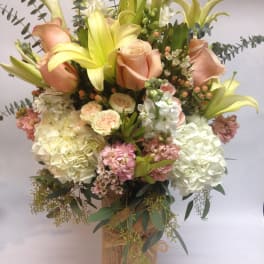 Bouquet of peach roses, yellow lilies, and white hydrangeas in a burlap-wrapped vase